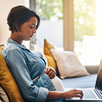 mujer embarazada usa una computadora portátil en el sofá