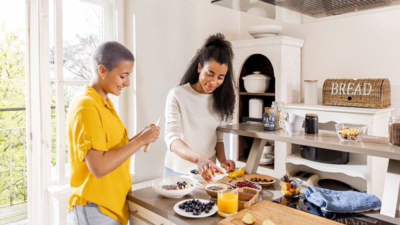 Dos mujeres jóvenes preparando un desayuno saludable en la cocina.