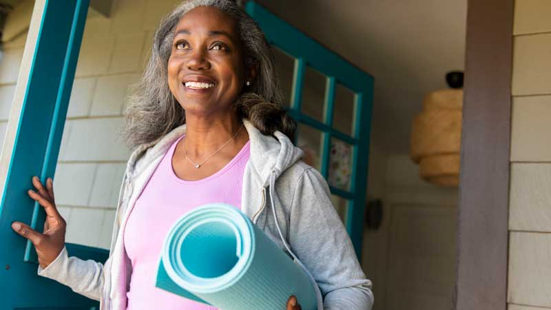 mujer saliendo de su casa con una colchoneta de yoga