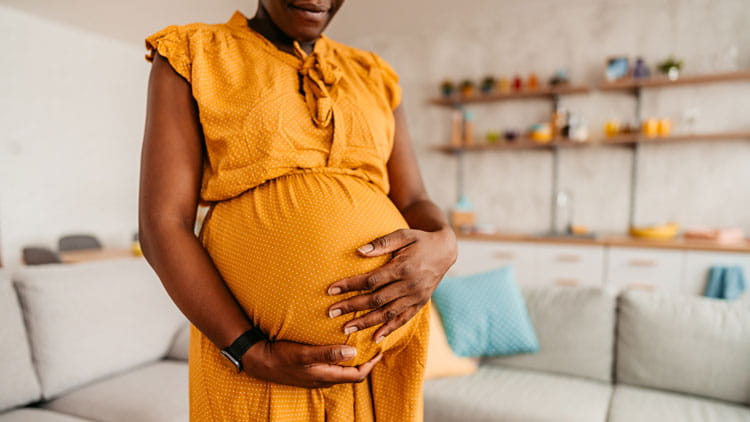 Pregnant woman at home in her living room cradling her pregnant belly.