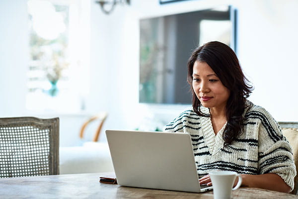 Mujer trabajando desde casa en una computadora portátil en la mesa de la cocina.