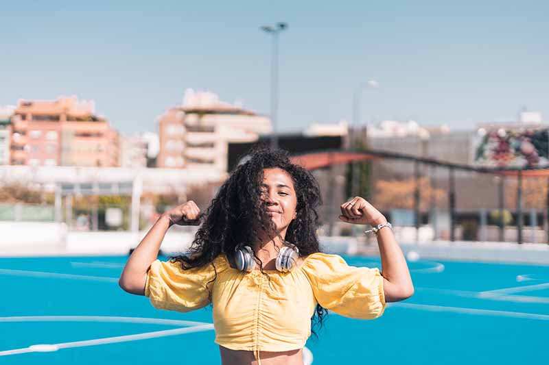 Niña afroamericana sonriendo con una camiseta amarilla levantando los brazos