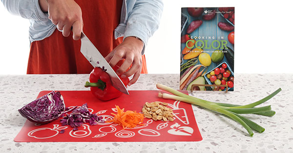 Cloe up of hands chopping vegetables on cutting board with American Heart Association Cooking in Color cookbook Cloe up of hands chopping vegetables on cutting board with American Heart Association Cooking in Color cookbook